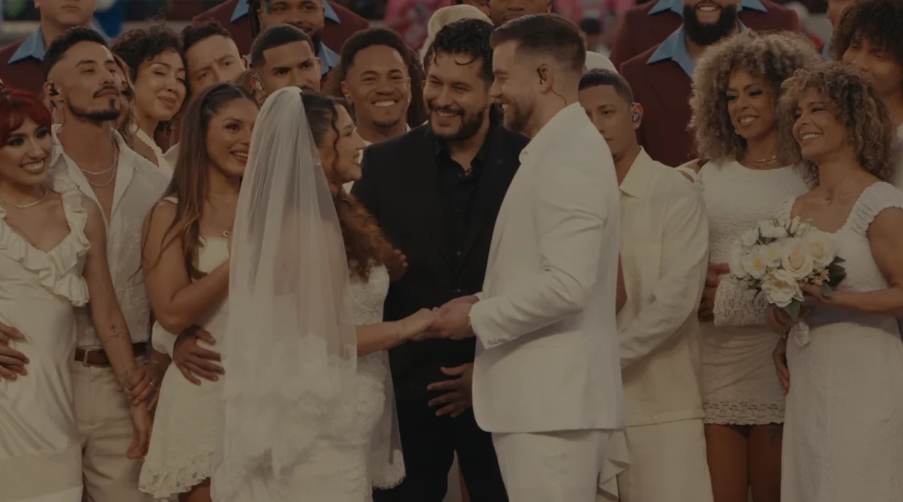 La boda real del show de Bad Bunny en el Super Bowl LX se convirtió en uno de los momentos más comentados del medio tiempo. Sobre el escenario del Levi’s Stadium, el artista puertorriqueño ofició como testigo de una ceremonia con plena validez legal, frente a millones de espectadores. La escena resumió el mensaje central del espectáculo: el poder del amor por encima de cualquier división. El show ya venía cargado de energía, con Bad Bunny alternando sus éxitos y clásicos del reguetón. Sin embargo, la atmósfera cambió cuando, tras una interpretación breve de “Mónaco”, las cámaras enfocaron a una pareja vestida de blanco rodeada de cortejo nupcial y músicos. El oficiante pronunció la frase clave, “ahora son marido y mujer”, y el estadio estalló en aplausos mientras los novios se besaban. ¿Quiénes se casaron en el show de Bad Bunny? La boda real del show de Bad Bunny fue planeada como una sorpresa, por eso los nombres de los novios no se hicieron públicos. Lo que sí trascendió es que la pareja había invitado al cantante a su ceremonia y que él respondió con una propuesta inesperada: celebrar la boda durante el espectáculo de medio tiempo del Super Bowl. Esa idea convirtió su unión en un momento histórico. De acuerdo con los representantes del artista, la ceremonia fue real y el matrimonio tiene validez legal, no fue solo una puesta en escena. Bad Bunny, vestido de blanco, firmó como testigo en el certificado de matrimonio, lo que le dio legitimidad al acto y reforzó el carácter simbólico de la boda. Sobre el escenario, los novios disfrutaron un pastel de varios niveles mientras el público seguía cada detalle. El gesto conectó con la narrativa del show, centrada en la unidad, la diversidad cultural y el amor como respuesta al odio. En un evento dominado por la competencia deportiva, la boda real del show de Bad Bunny añadió un capítulo íntimo y emotivo. ¿Cómo se integró la boda real al espectáculo del Super Bowl? La boda real del show de Bad Bunny no fue un momento aislado, sino parte de una coreografía cuidadosamente construida. Después de “Mónaco”, el escenario se transformó en una suerte de salón de fiesta, con luces cálidas, músicos en vivo y el cortejo nupcial acompañando cada paso. El anuncio del oficiante dio paso al beso, al pastel y a un mini “primer baile” observado por el mundo. En ese punto, apareció Lady Gaga, otra de las grandes sorpresas de la noche. La artista interpretó “Die With a Smile” junto a una banda en vivo, mientras el reguetonero y los recién casados se movían al centro del escenario. Bad Bunny animó a la pareja a un “baile inolvidable” y, visiblemente emocionado, gritó “¡baile, baile, baile!” mientras bailarines rodeaban el círculo principal. La boda real del show de Bad Bunny se mezcló así con la fiesta musical. Hubo incluso gestos más íntimos, como el momento en que el cantante bailó con una niña pequeña y despertó a un niño que dormía en las sillas, imagen que conmovió especialmente a espectadores latinoamericanos. Todo reforzó la sensación de estar presenciando una celebración familiar en medio de un evento global. ¿Qué otros artistas acompañaron a Bad Bunny en el medio tiempo? La boda real del show de Bad Bunny fue solo una pieza de un espectáculo lleno de invitados. Sobre el escenario aparecieron figuras como Pedro Pascal, Cardi B, Jessica Alba y Karol G, que se sumaron a la coreografía general. Ricky Martin también tuvo un rol destacado al interpretar líneas de “Lo que le pasó a Hawái”, tema incluido en el álbum más reciente del puertorriqueño. El repertorio de Bad Bunny combinó canciones como “Tití Me Preguntó”, “Yo Perreo Sola”, “Voy a llevarte pa’ PR” y “NuevaYol”, junto a fragmentos emblemáticos de la música urbana. Hubo guiños a temas como “Pa que retozen” de Tego Calderón, “Dale Don Dale” de Don Omar y “Gasolina” de Daddy Yankee, lo que convirtió el medio tiempo en un homenaje directo a la historia del reguetón. La presencia de la banda de salsa puertorriqueña Los Sobrinos añadió una capa adicional de sabor caribeño, reforzando la identidad cultural del espectáculo. En ese contexto, la boda real del show de Bad Bunny encajó como un clímax emocional dentro de una gran celebración latina. ¿Qué mensaje dejó la boda real del show de Bad Bunny? Más allá del espectáculo, la boda real del show de Bad Bunny se leyó como parte de un mensaje social y cultural. En uno de los momentos finales, mientras se veían banderas de distintos países, una gran pantalla mostró la frase “Lo único más poderoso que el odio es el amor”. Esa declaración terminó de unir la ceremonia nupcial con el discurso de unidad que atravesó todo el medio tiempo. Luego, el artista tomó un balón de fútbol americano con la inscripción “Juntos somos América” y lo lanzó al aire, reforzando la idea de un continente diverso, pero conectado por raíces y emociones comunes. La boda real del show de Bad Bunny, en ese sentido, funcionó como metáfora de encuentro y comunidad frente a un público global. En la rueda de prensa previa, el propio cantante había adelantado que su presentación sería “una fiesta enorme” donde la gente solo debía preocuparse por bailar y disfrutar, sin importar el idioma. La boda real del show de Bad Bunny cumplió esa promesa y, al mismo tiempo, dejó una imagen difícil de repetir: una unión legal celebrada en vivo, en el escenario deportivo más visto del mundo, con la música latina como banda sonora.