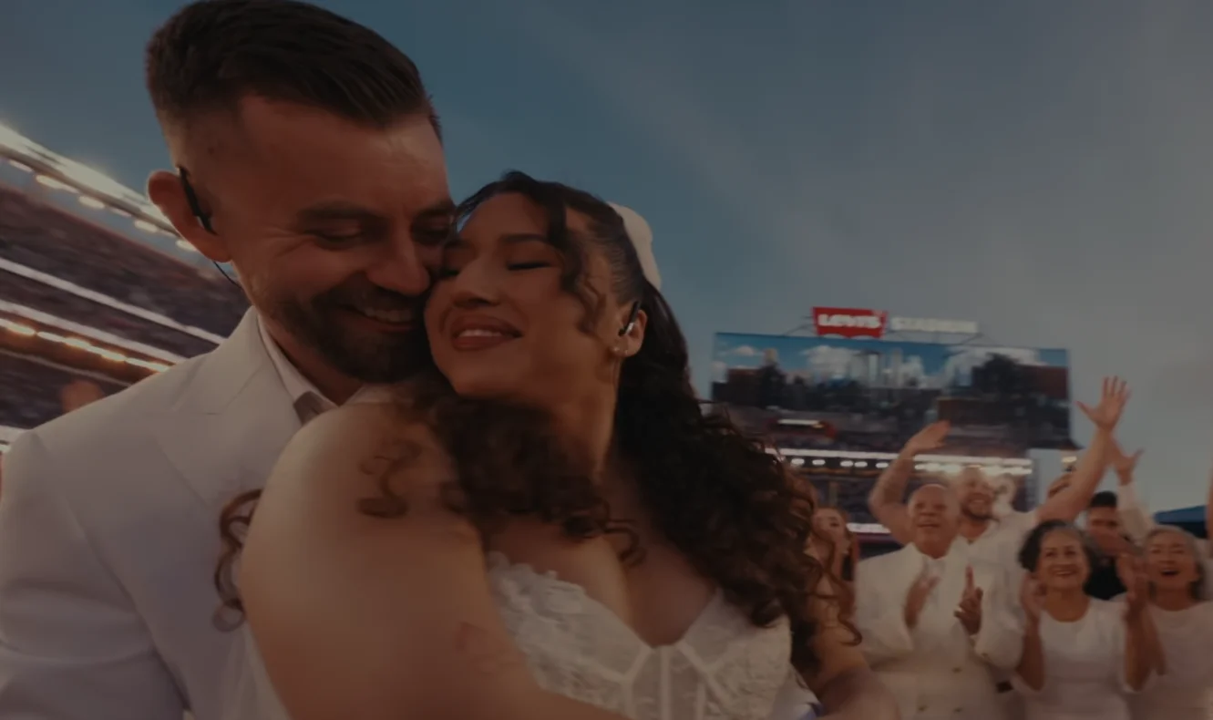 La boda real del show de Bad Bunny en el Super Bowl LX se convirtió en uno de los momentos más comentados del medio tiempo. Sobre el escenario del Levi’s Stadium, el artista puertorriqueño ofició como testigo de una ceremonia con plena validez legal, frente a millones de espectadores. La escena resumió el mensaje central del espectáculo: el poder del amor por encima de cualquier división. El show ya venía cargado de energía, con Bad Bunny alternando sus éxitos y clásicos del reguetón. Sin embargo, la atmósfera cambió cuando, tras una interpretación breve de “Mónaco”, las cámaras enfocaron a una pareja vestida de blanco rodeada de cortejo nupcial y músicos. El oficiante pronunció la frase clave, “ahora son marido y mujer”, y el estadio estalló en aplausos mientras los novios se besaban. ¿Quiénes se casaron en el show de Bad Bunny? La boda real del show de Bad Bunny fue planeada como una sorpresa, por eso los nombres de los novios no se hicieron públicos. Lo que sí trascendió es que la pareja había invitado al cantante a su ceremonia y que él respondió con una propuesta inesperada: celebrar la boda durante el espectáculo de medio tiempo del Super Bowl. Esa idea convirtió su unión en un momento histórico. De acuerdo con los representantes del artista, la ceremonia fue real y el matrimonio tiene validez legal, no fue solo una puesta en escena. Bad Bunny, vestido de blanco, firmó como testigo en el certificado de matrimonio, lo que le dio legitimidad al acto y reforzó el carácter simbólico de la boda. Sobre el escenario, los novios disfrutaron un pastel de varios niveles mientras el público seguía cada detalle. El gesto conectó con la narrativa del show, centrada en la unidad, la diversidad cultural y el amor como respuesta al odio. En un evento dominado por la competencia deportiva, la boda real del show de Bad Bunny añadió un capítulo íntimo y emotivo. ¿Cómo se integró la boda real al espectáculo del Super Bowl? La boda real del show de Bad Bunny no fue un momento aislado, sino parte de una coreografía cuidadosamente construida. Después de “Mónaco”, el escenario se transformó en una suerte de salón de fiesta, con luces cálidas, músicos en vivo y el cortejo nupcial acompañando cada paso. El anuncio del oficiante dio paso al beso, al pastel y a un mini “primer baile” observado por el mundo. En ese punto, apareció Lady Gaga, otra de las grandes sorpresas de la noche. La artista interpretó “Die With a Smile” junto a una banda en vivo, mientras el reguetonero y los recién casados se movían al centro del escenario. Bad Bunny animó a la pareja a un “baile inolvidable” y, visiblemente emocionado, gritó “¡baile, baile, baile!” mientras bailarines rodeaban el círculo principal. La boda real del show de Bad Bunny se mezcló así con la fiesta musical. Hubo incluso gestos más íntimos, como el momento en que el cantante bailó con una niña pequeña y despertó a un niño que dormía en las sillas, imagen que conmovió especialmente a espectadores latinoamericanos. Todo reforzó la sensación de estar presenciando una celebración familiar en medio de un evento global. ¿Qué otros artistas acompañaron a Bad Bunny en el medio tiempo? La boda real del show de Bad Bunny fue solo una pieza de un espectáculo lleno de invitados. Sobre el escenario aparecieron figuras como Pedro Pascal, Cardi B, Jessica Alba y Karol G, que se sumaron a la coreografía general. Ricky Martin también tuvo un rol destacado al interpretar líneas de “Lo que le pasó a Hawái”, tema incluido en el álbum más reciente del puertorriqueño. El repertorio de Bad Bunny combinó canciones como “Tití Me Preguntó”, “Yo Perreo Sola”, “Voy a llevarte pa’ PR” y “NuevaYol”, junto a fragmentos emblemáticos de la música urbana. Hubo guiños a temas como “Pa que retozen” de Tego Calderón, “Dale Don Dale” de Don Omar y “Gasolina” de Daddy Yankee, lo que convirtió el medio tiempo en un homenaje directo a la historia del reguetón. La presencia de la banda de salsa puertorriqueña Los Sobrinos añadió una capa adicional de sabor caribeño, reforzando la identidad cultural del espectáculo. En ese contexto, la boda real del show de Bad Bunny encajó como un clímax emocional dentro de una gran celebración latina. ¿Qué mensaje dejó la boda real del show de Bad Bunny? Más allá del espectáculo, la boda real del show de Bad Bunny se leyó como parte de un mensaje social y cultural. En uno de los momentos finales, mientras se veían banderas de distintos países, una gran pantalla mostró la frase “Lo único más poderoso que el odio es el amor”. Esa declaración terminó de unir la ceremonia nupcial con el discurso de unidad que atravesó todo el medio tiempo. Luego, el artista tomó un balón de fútbol americano con la inscripción “Juntos somos América” y lo lanzó al aire, reforzando la idea de un continente diverso, pero conectado por raíces y emociones comunes. La boda real del show de Bad Bunny, en ese sentido, funcionó como metáfora de encuentro y comunidad frente a un público global. En la rueda de prensa previa, el propio cantante había adelantado que su presentación sería “una fiesta enorme” donde la gente solo debía preocuparse por bailar y disfrutar, sin importar el idioma. La boda real del show de Bad Bunny cumplió esa promesa y, al mismo tiempo, dejó una imagen difícil de repetir: una unión legal celebrada en vivo, en el escenario deportivo más visto del mundo, con la música latina como banda sonora.